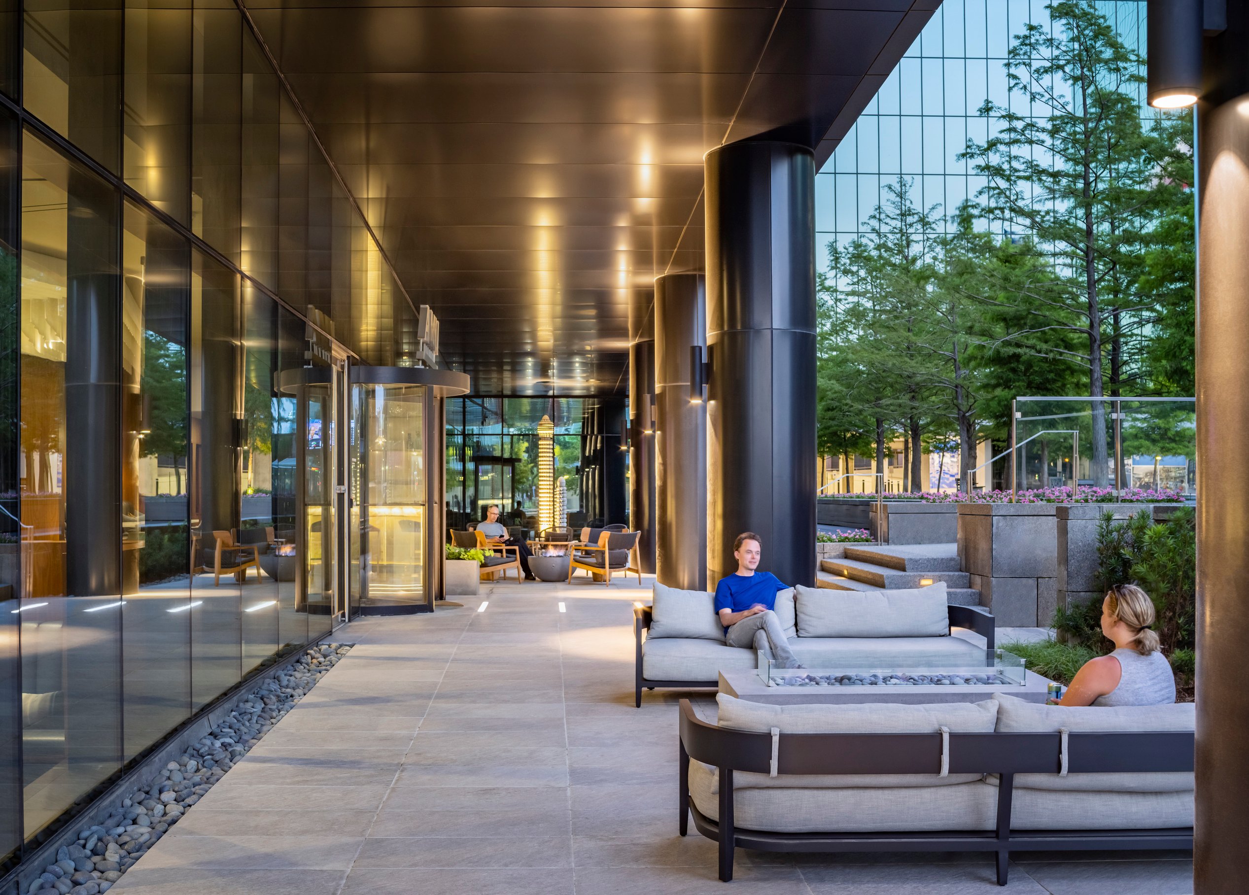 A quiet covered outdoor seating area with low-slung couches and landscaping.