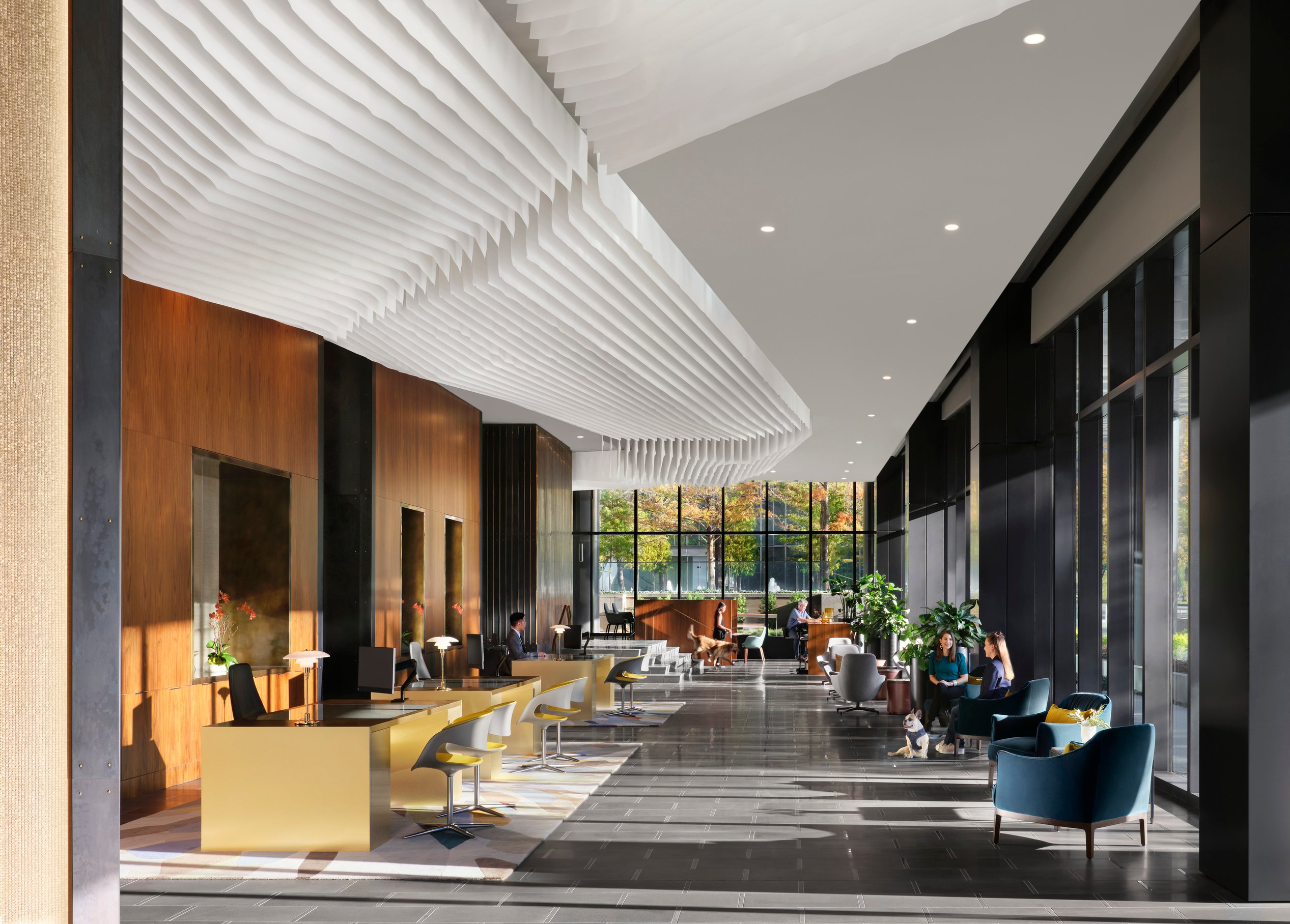 A lobby of a modern high-rise building featuring an angled ceiling with comfortable seating and large floor-to-ceiling windows.