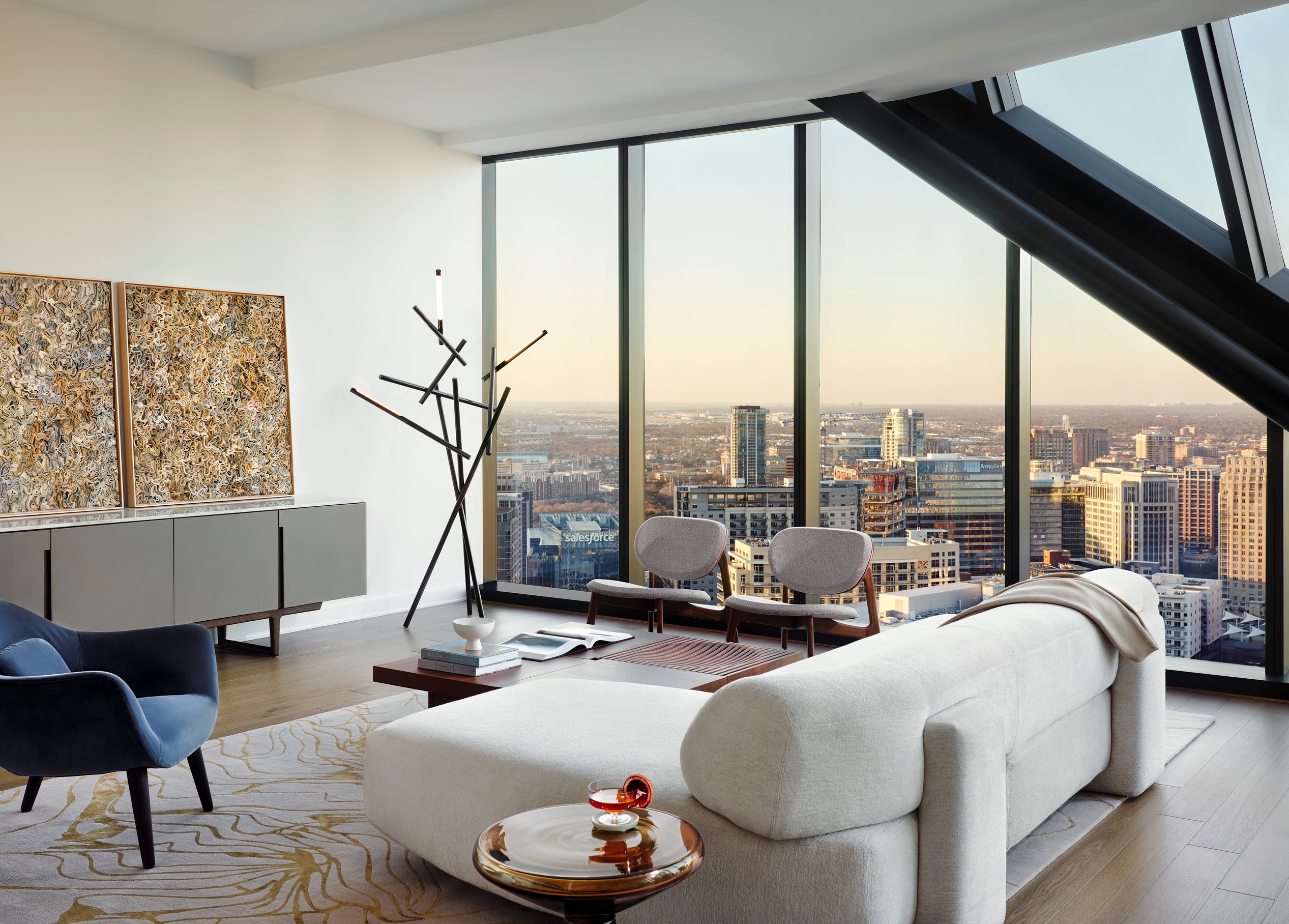 An open and airy living area in a modern high-rise with a large white couch near a floor-to-ceiling window.