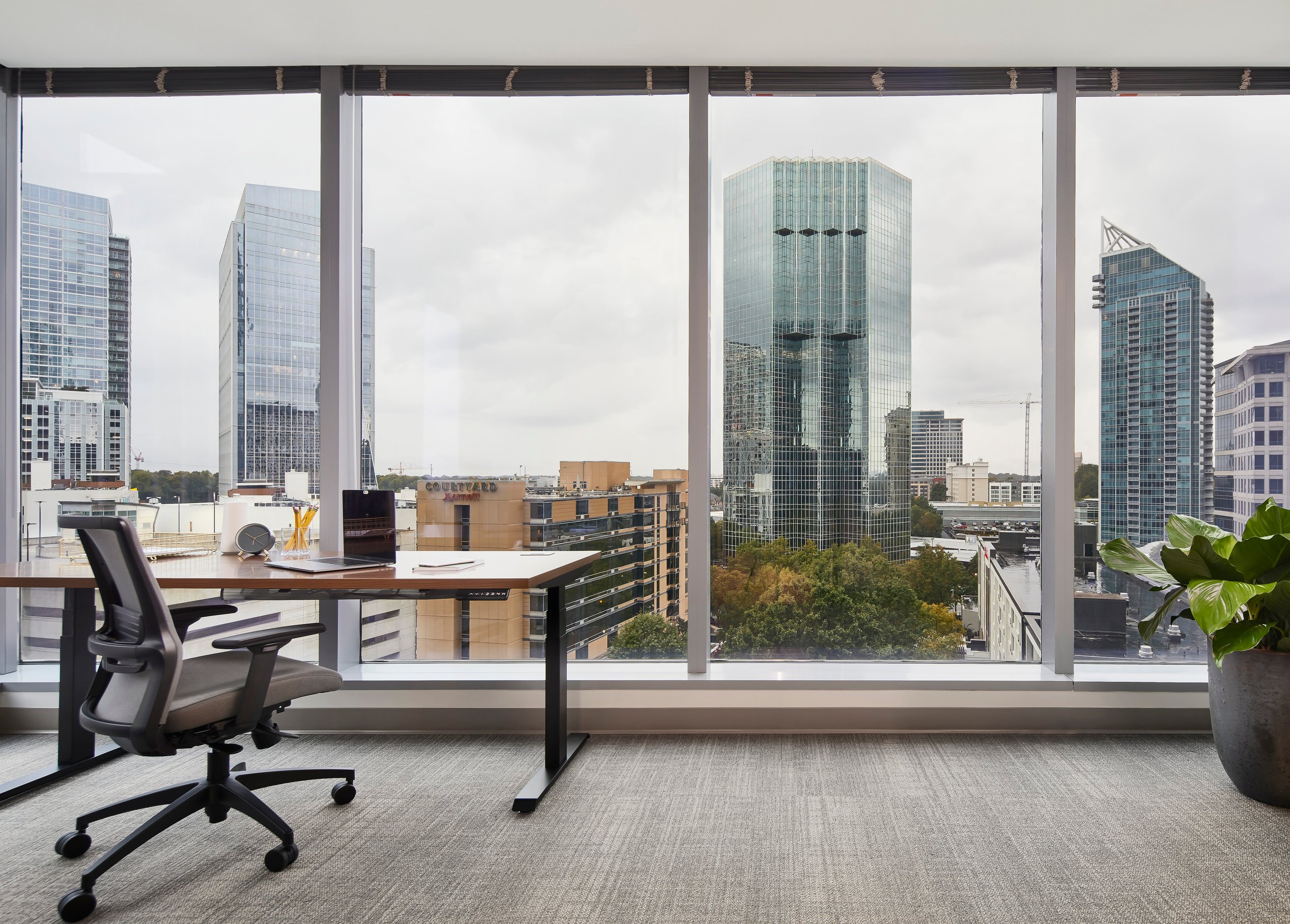 A modern office space with a single desk and chair overlooking multiple high rises in the distance.